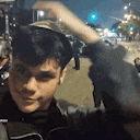 a young man is standing on a city street at night holding his hand to his head .