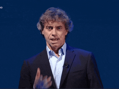 a man in a suit stands in front of a blue background and the word hd is on the bottom right