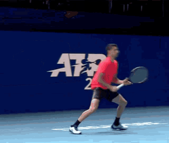 a man in a red shirt is holding a tennis racquet in front of a sign that says atp
