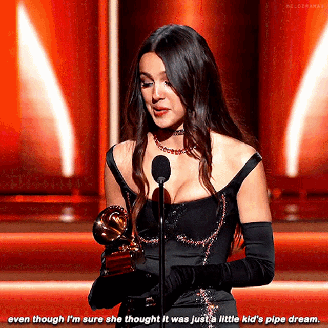 a woman in a black dress is standing in front of a microphone and holding a trophy ..