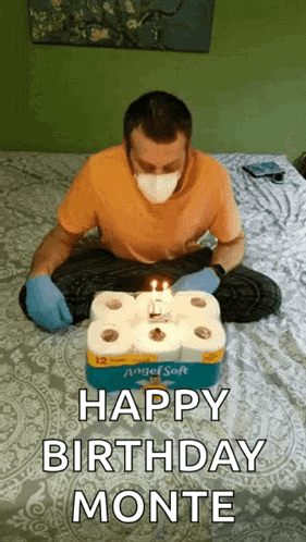 a man wearing a mask is sitting on a bed with a birthday cake made out of toilet paper .
