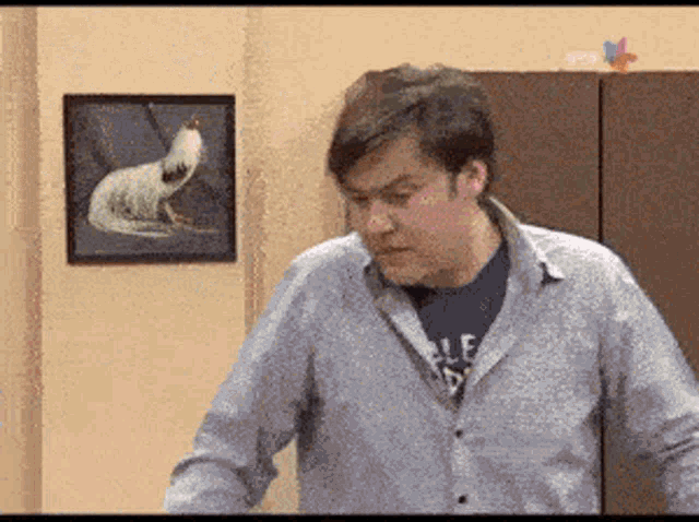 a man in a blue shirt is standing in front of a painting of a chicken