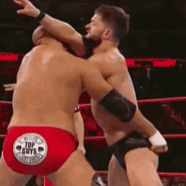 two men are wrestling in a ring and one of them is wearing a red underwear .