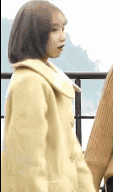 a woman in a yellow coat is standing next to another woman in a brown sweater