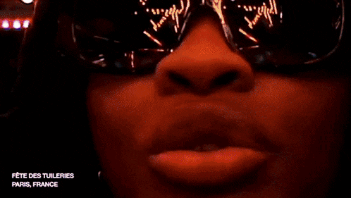 a man wearing sunglasses and a hood stands in front of a ferris wheel at night
