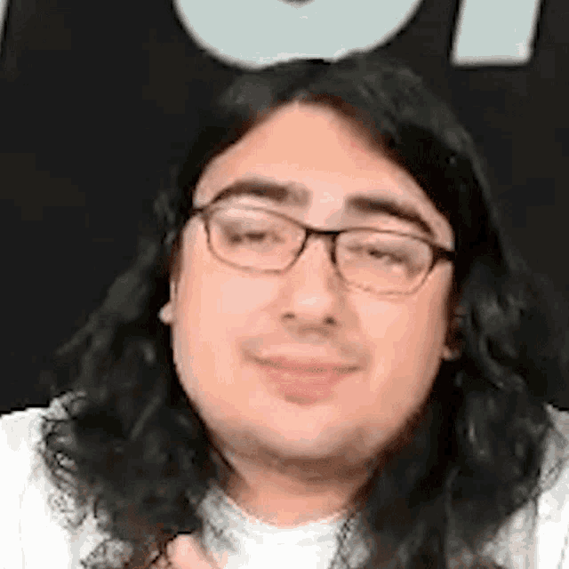 a man with long hair and glasses is smiling in front of a black background .