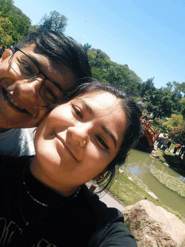 a man and a woman are posing for a picture in front of a pond and bridge
