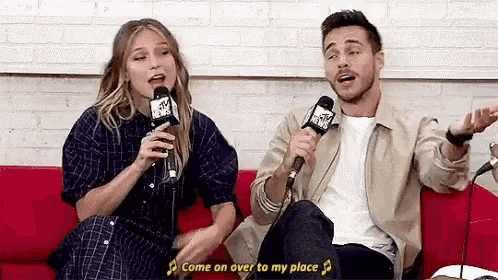 a man and a woman singing into microphones on a red couch .