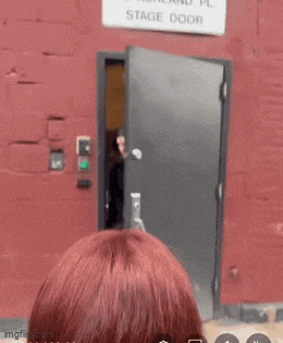 a woman stands in front of a stage door that is labeled 212 ashland pl