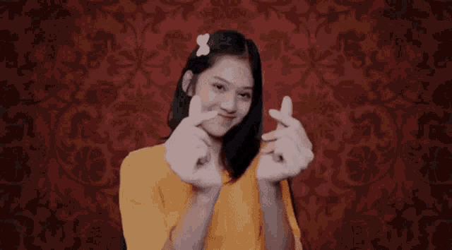 a girl in a yellow shirt is making a heart shape with her fingers