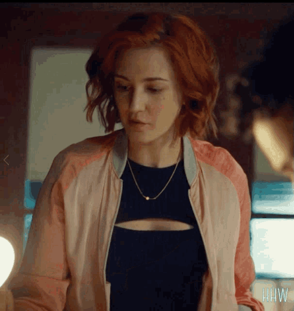 a woman with red hair is wearing a pink jacket and black top