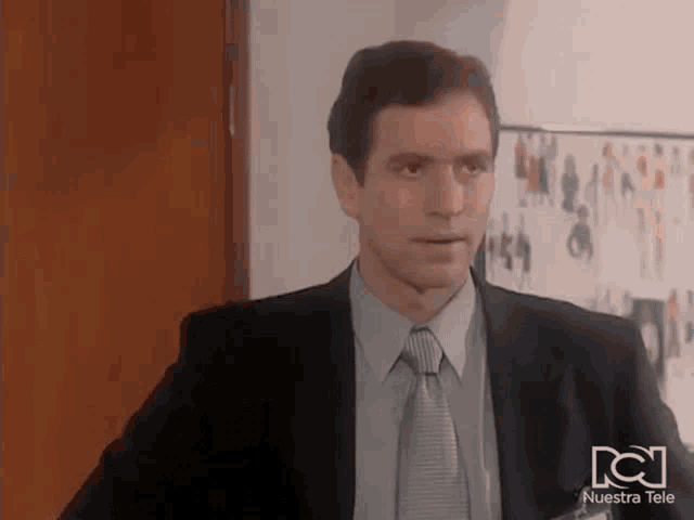 a man in a suit and tie is standing in front of a wall with pictures of people .