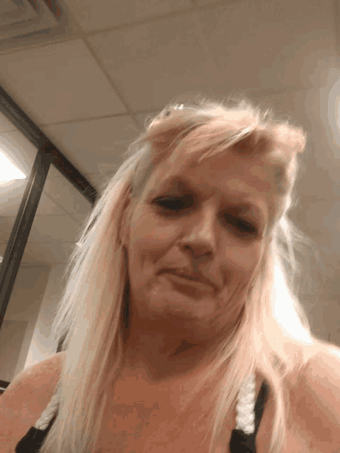 a woman with blonde hair and a black tank top looks at the camera