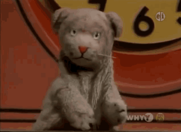 a stuffed animal is sitting in front of a clock that says why 7