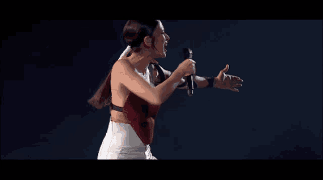 a woman singing into a microphone with her arms outstretched in the dark