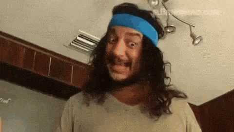 a man with long hair and a blue headband is making a face .