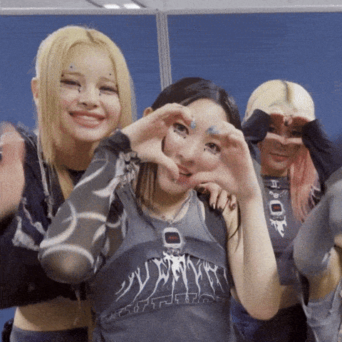 a girl wearing a tank top that says ' nct ' on it makes a heart shape with her hands