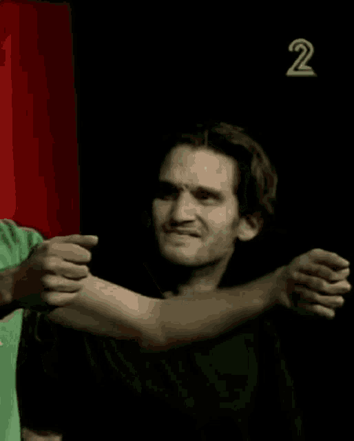 a man in a green shirt is hugging another man in a black shirt with the number 2 behind him