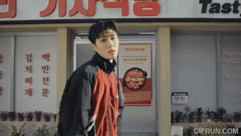 a man in a red jacket stands in front of a restaurant called tasty
