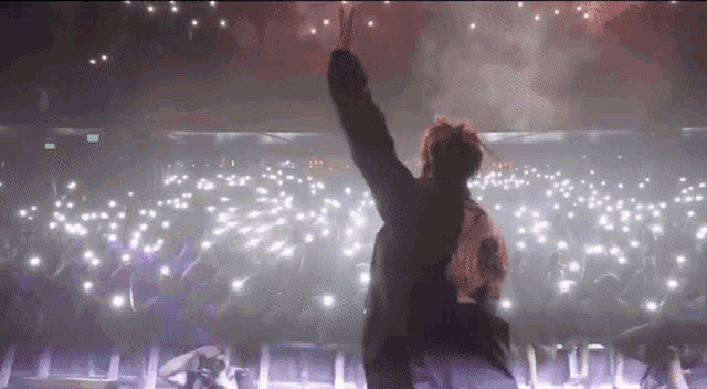 a man is standing on a stage with his arms outstretched in front of a crowd of people .