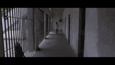 a man is walking down a hallway in a jail cell with bars .