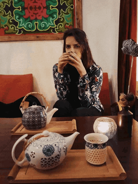 a woman sits at a table with a teapot and cups on it
