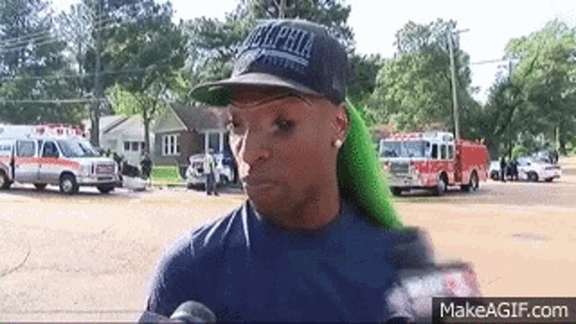 a woman with green hair is wearing a black hat and talking to a reporter .