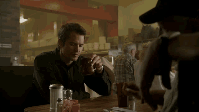 a man sits at a table in a diner drinking from a mug