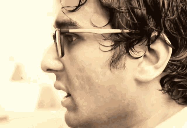 a man with curly hair wearing glasses looks to the side