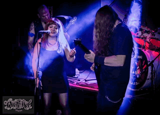 a man playing a guitar and a woman singing in front of a drum set that says dog