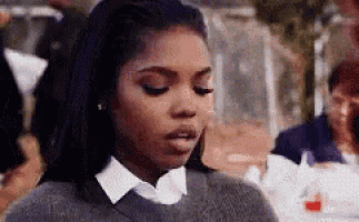 a woman wearing a sweater and a white collared shirt is looking at the camera .