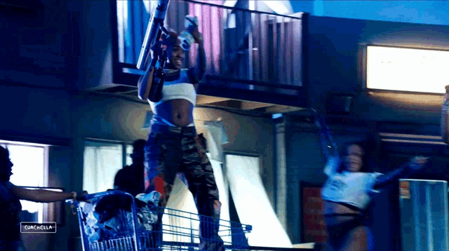 a woman in a crop top is standing on a shopping cart with a sign behind her that says campbells
