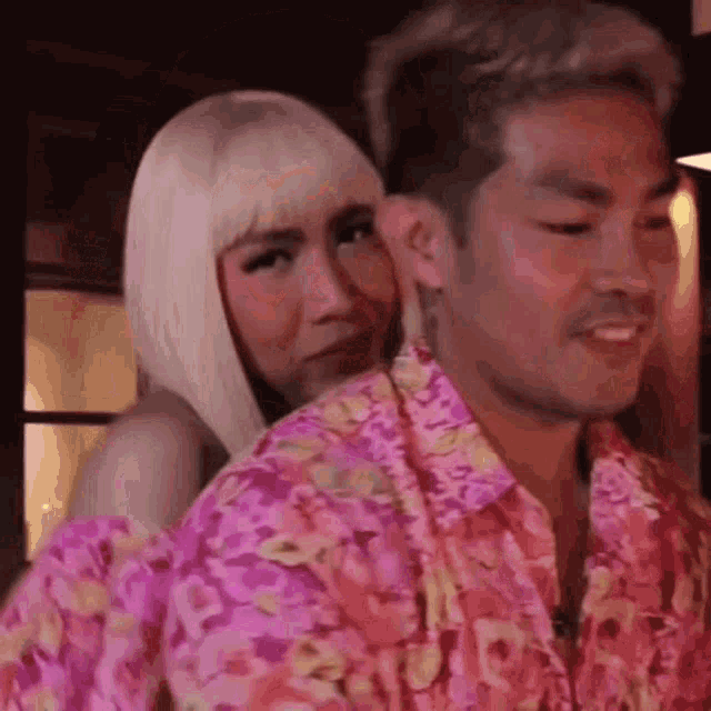 a man and a woman are standing next to each other . the woman is wearing a pink floral shirt .