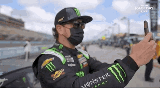 a man wearing a monster shirt is taking a picture of himself with his cell phone .