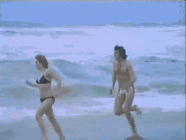 a man and a woman in a bikini are running on the beach
