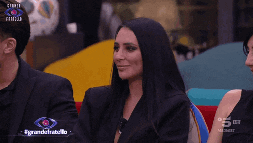 a woman sits in front of a sign that says #grandefratello