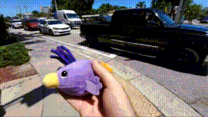 a person is holding a stuffed purple bird with a yellow beak in their hand