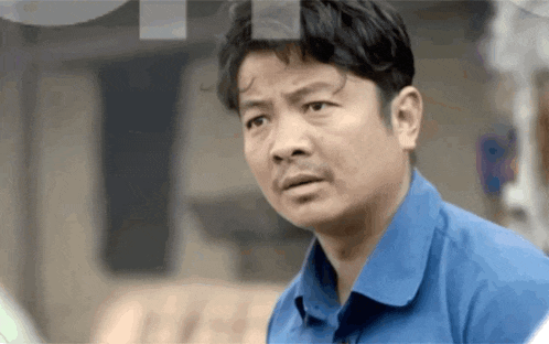 a man in a blue shirt is looking at the camera and making a funny face .