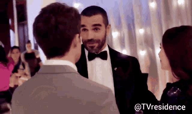 a man in a tuxedo and bow tie is talking to a woman .