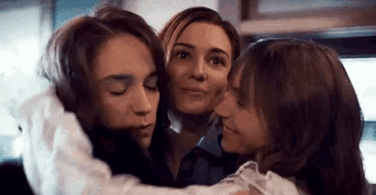 a group of three women are hugging each other and smiling .