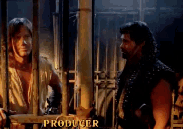 two men are standing next to each other in a cage and the word producer is on the bottom of the screen .