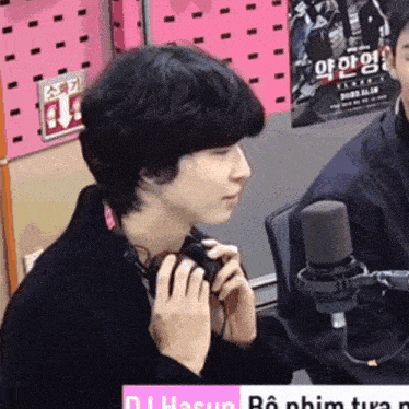 a man wearing headphones is talking into a microphone in front of a sign that says ' dj hasun '