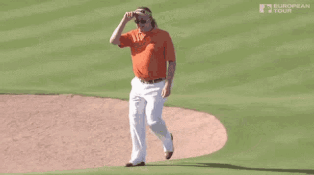 a man in an orange shirt is walking on a golf course holding a golf club .