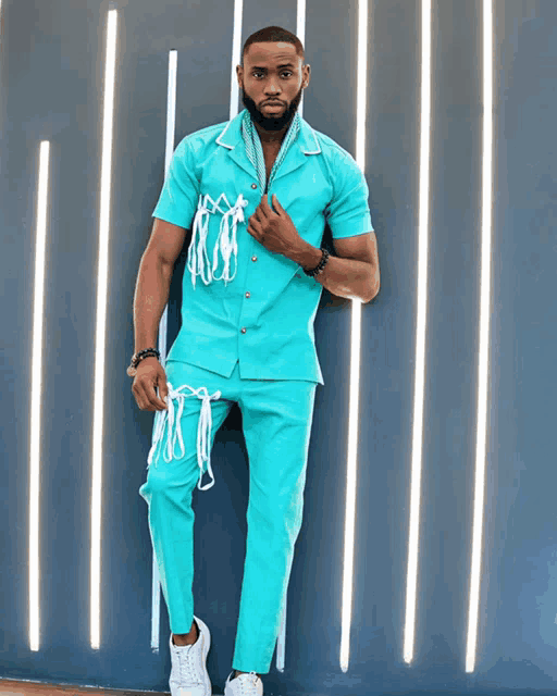 a man in a teal shirt and pants stands in front of a wall