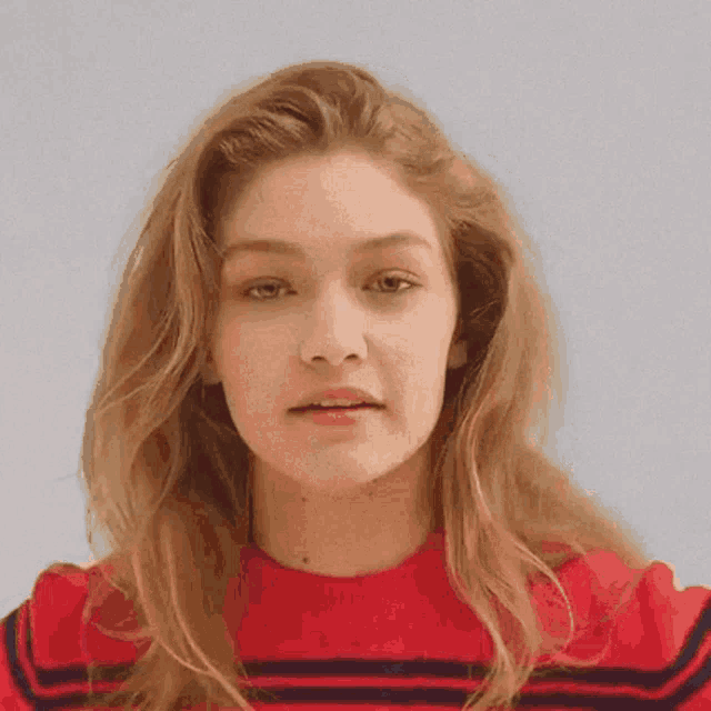 a close up of a woman 's face wearing a red sweater and making a funny face .