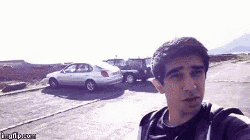 a man is taking a selfie in front of a parking lot with cars parked in the background .