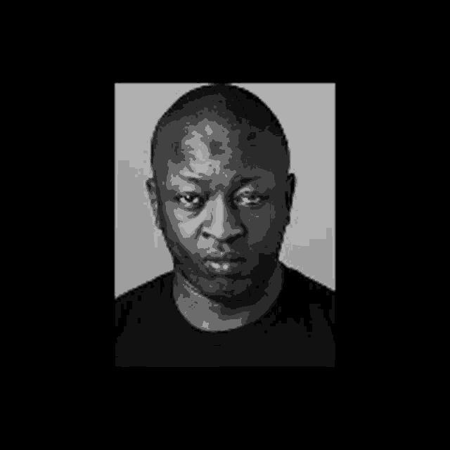 a black and white photo of a man wearing a black shirt looking at the camera .