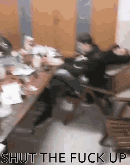 a blurry picture of people sitting around a table with the words shut the fuck up written in the corner