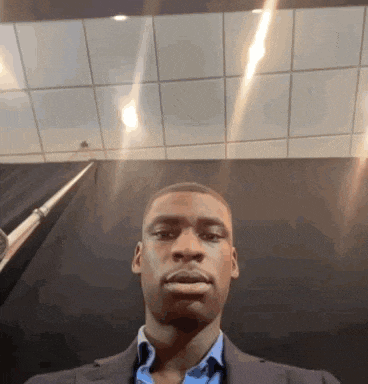 a man in a suit takes a selfie in front of a black curtain