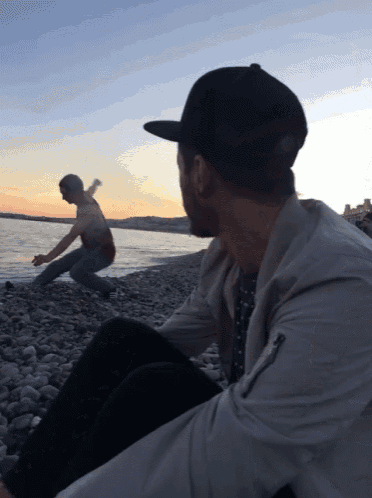a man wearing a baseball cap sits on a rocky beach